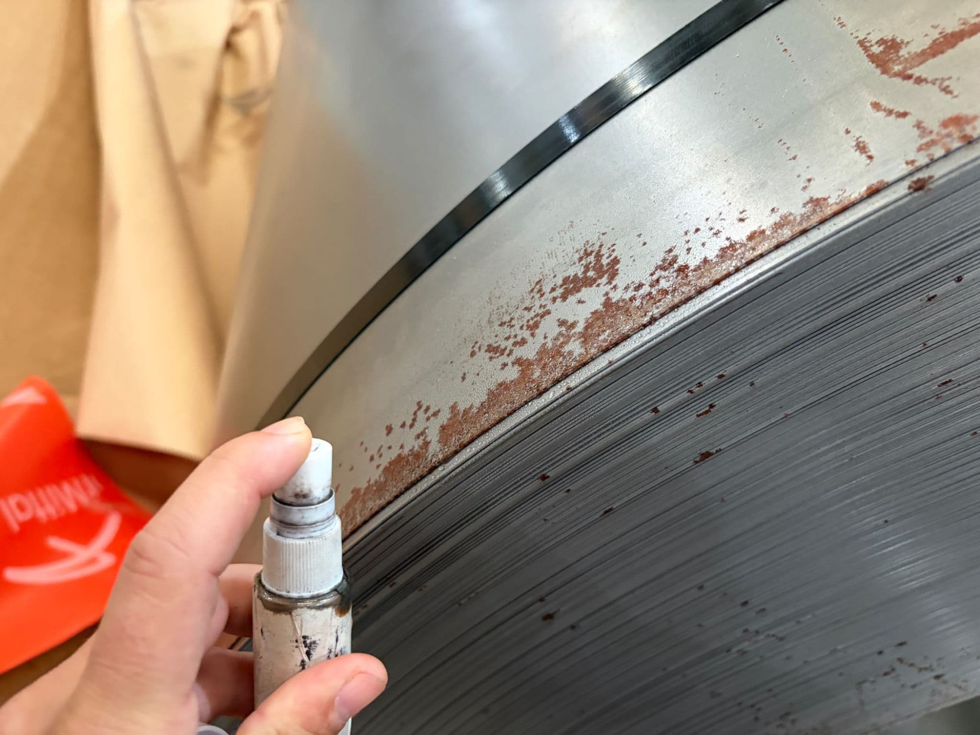 Checking rust marks concentrated along the wrap edge. Findings are photographed and recorded against the coil number, documenting the condition before loading.